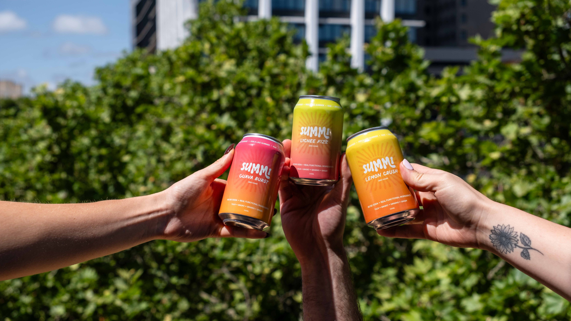 Three people holding colourful cans with 'SUMMi' branding against a green outdoor background.