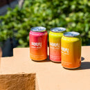 Three colorful cans of SUMMi drinks on a stone surface with greenery in the background