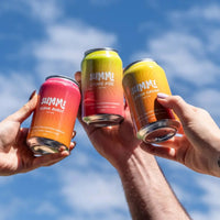 Three cans of SUMMi soda held aloft against a blue sky
