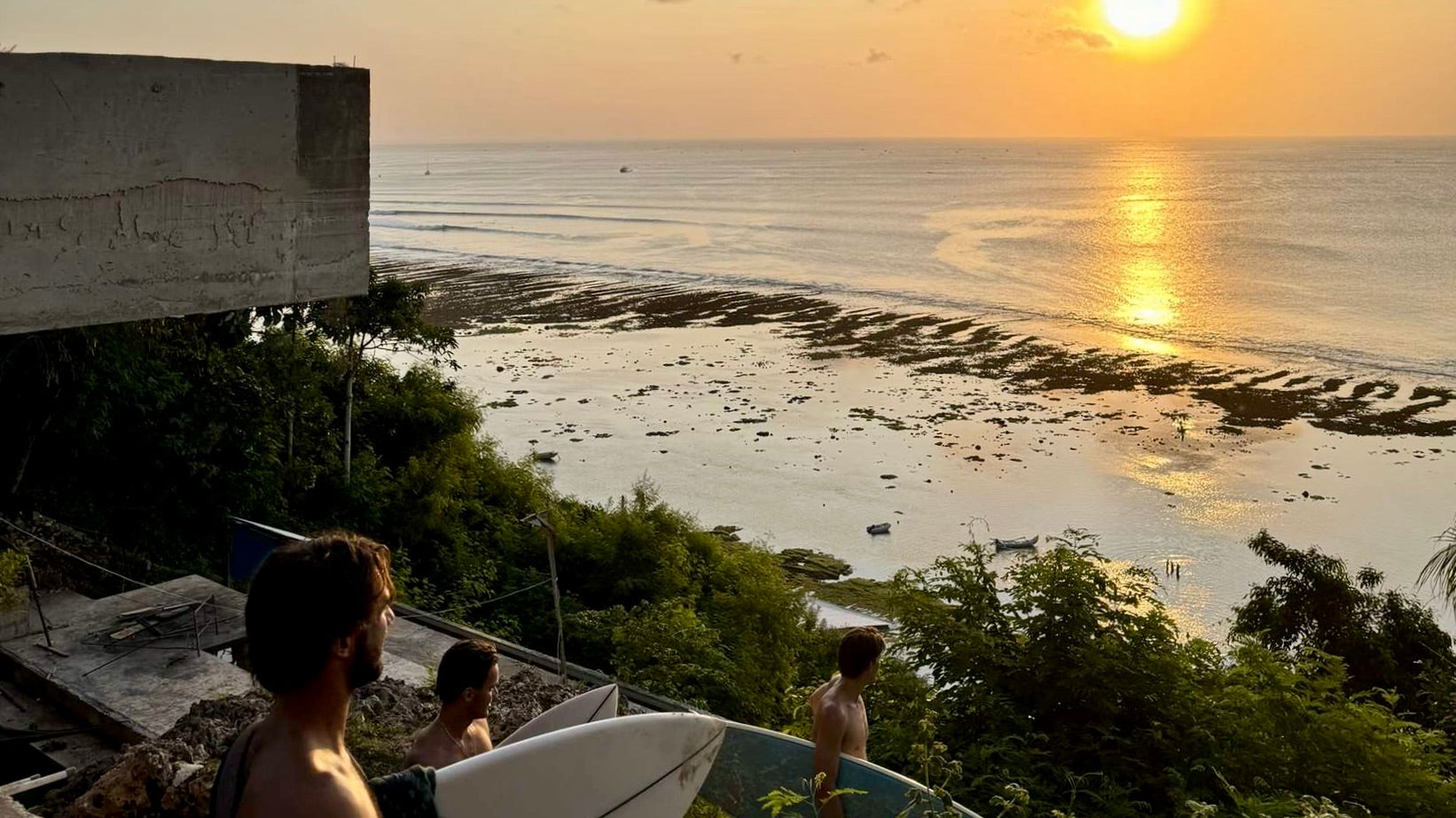 People with surfboards overlooking a sunset over the ocean from a high vantage point.